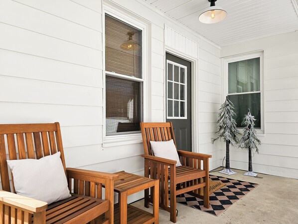 A porch with two wooden chairs and a bench, a small table, and a decorative tree.