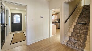 A hallway with a wooden floor, a dark front door, and a staircase with a 'Watch Your Head' sign. - NEW! Hot Tub, Firepit & Game System Near Hershey - Walk To Lake & Fishing! (Lebanon)