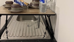 Una cocina con un lavamanos, una encimera con una botella de agua y algunos platos.