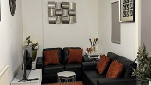 Una sala de estar moderna con un sofá de cuero negro, una mesa de centro blanca y una mesa de comedor negra con platos y una copa de vino.