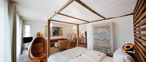 Habitación de hotel moderna con cama a dosel, una silla colgante, un escritorio y vistas de la ciudad.