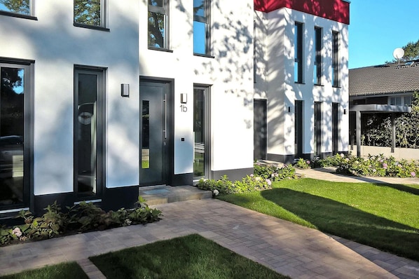 En moderne bygning med en hvid facade, vinduer med sorte rammer, og et rødt detaljeøje øverst til højre.