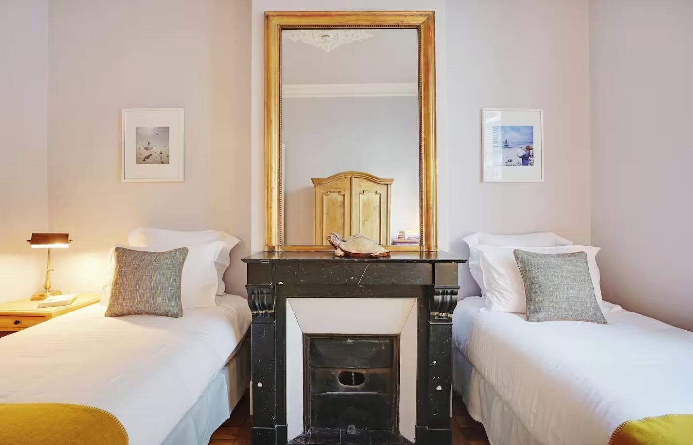A room with two single beds, a large mirror, and a fireplace.