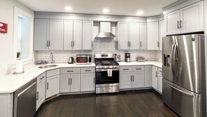 Una cocina moderna con armarios blancos, electrodomésticos de acero inoxidable y piso de madera oscura.