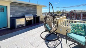 Una terraza en la azotea con una silla colgante, un sofá y una parrilla.