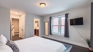 Un dormitorio con una cama grande, un televisor montado en la pared y una ventana con cortinas.