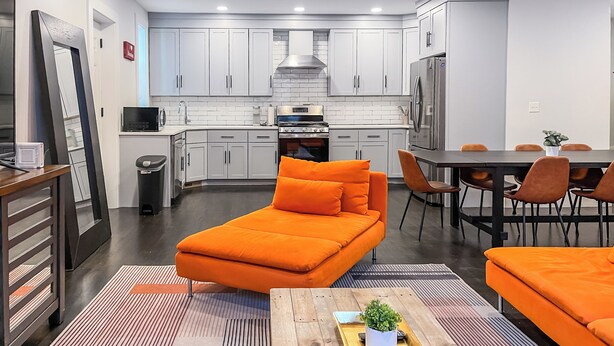 Una cocina moderna con armarios blancos, un refrigerador de acero inoxidable y un comedor con mobiliario naranja.