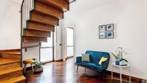 Un saló modern amb una escala de fusta, un sofà blau i una taula auxiliar petita amb una planta.