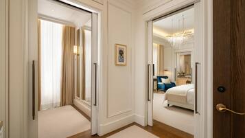 A hotel corridor with a carpeted floor, a framed picture on the wall, and a bed with a blue headboard in the adjacent room.