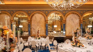 Un salón de banquetes lujoso con candelabros ornamentados, paredes de mármol y mesas elegantemente dispuestas.