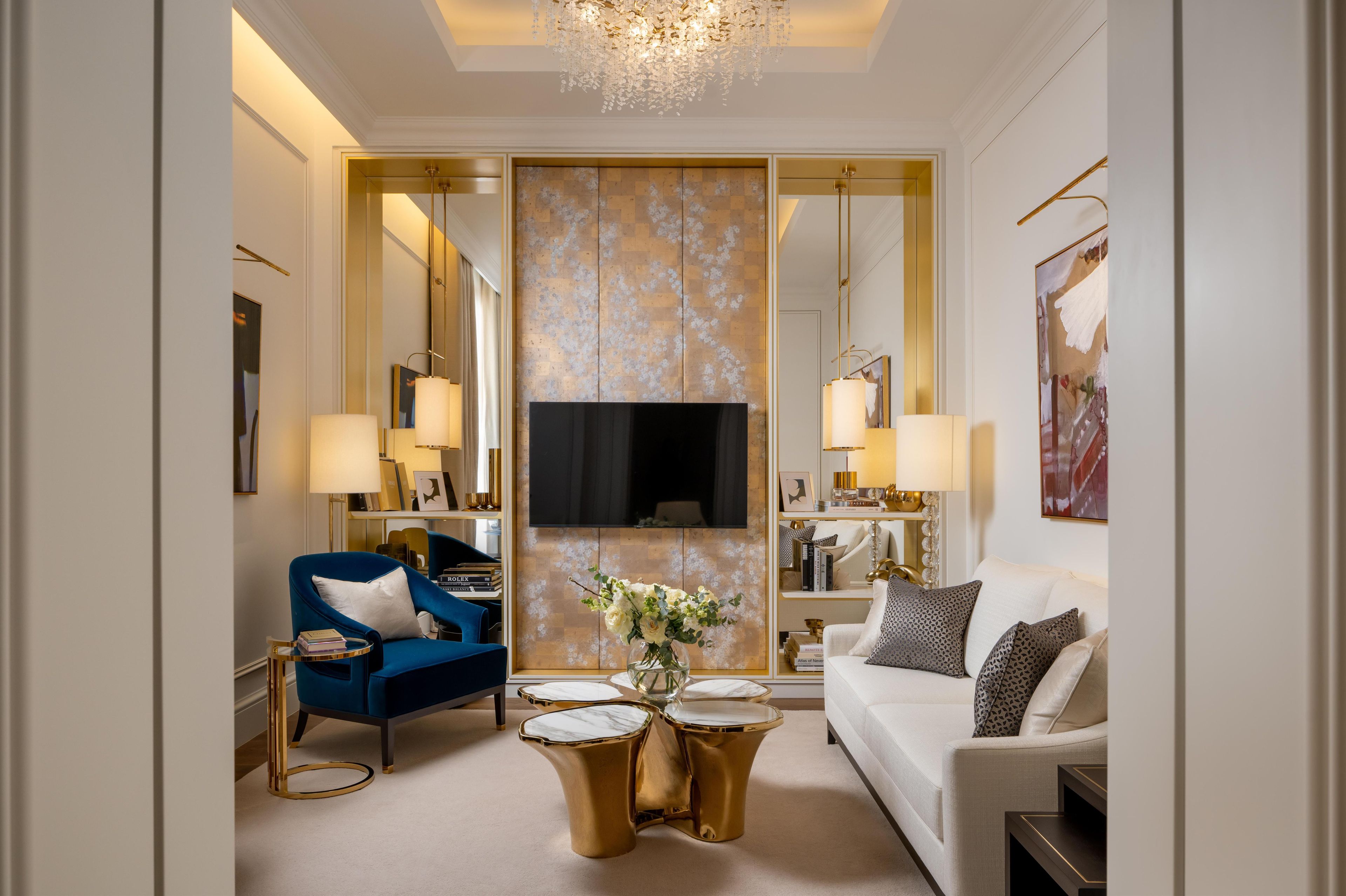 Un salon moderne avec un fauteuil bleu, un canapé blanc et des tables d’appoint dorées.