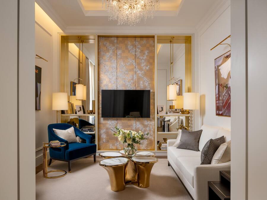 Un salon moderne avec un fauteuil bleu, un canapé blanc et des tables d’appoint dorées.