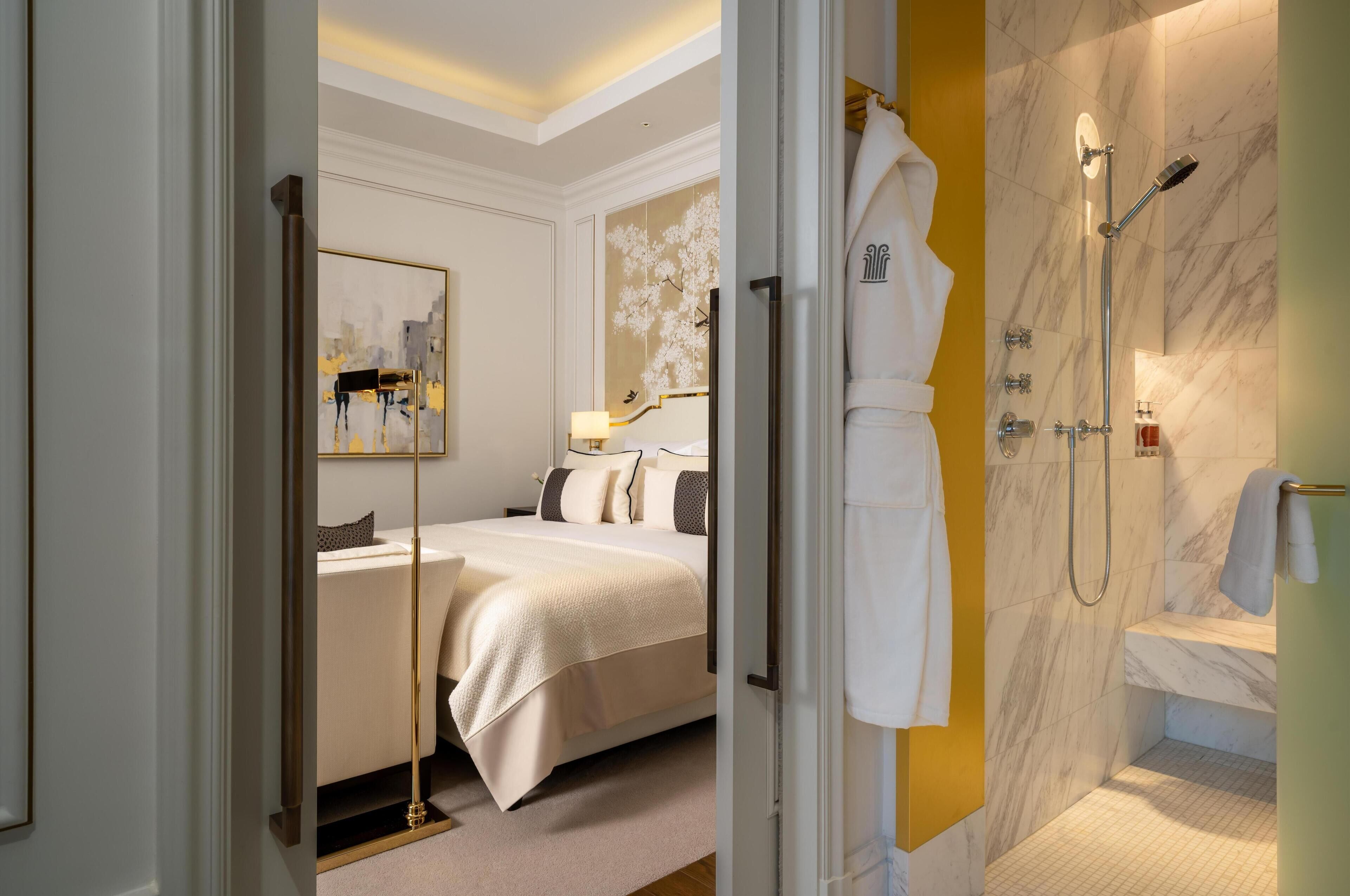 A hotel room with a bed, a bathroom with a shower, and a mirror.