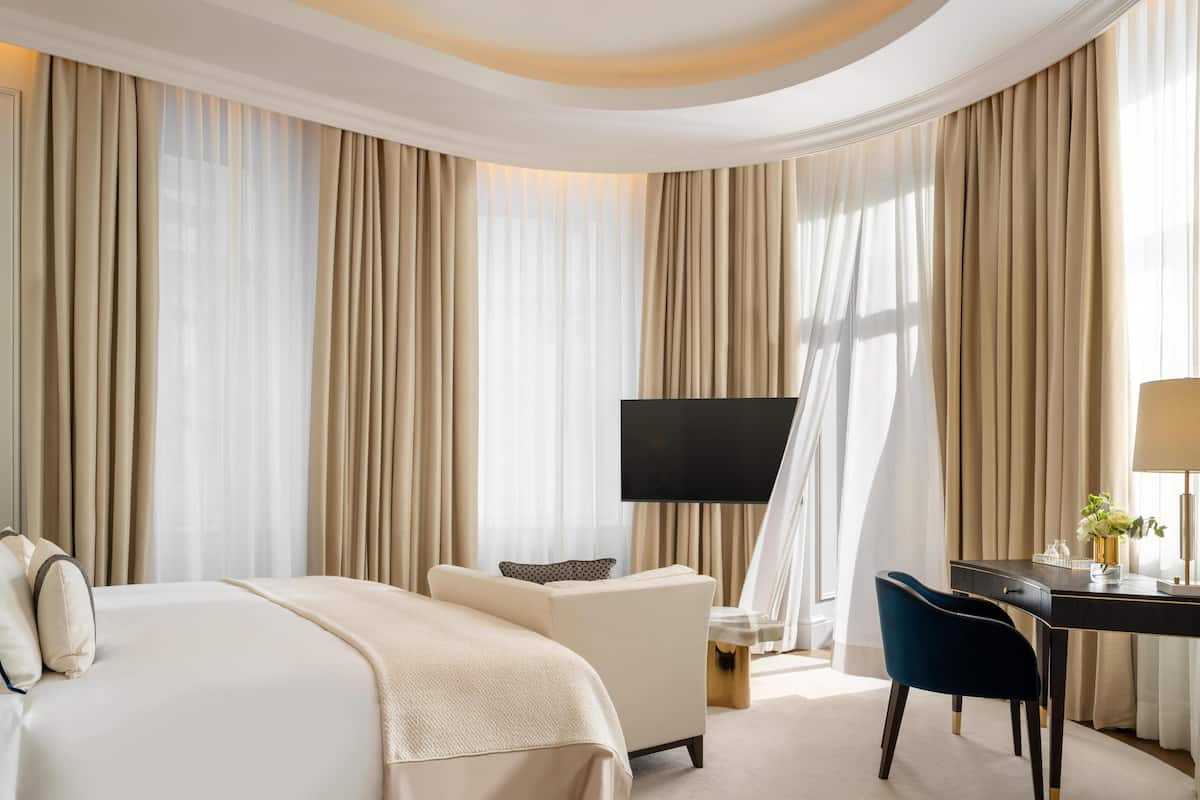 Une chambre d’hôtel avec un grand lit, un bureau, une chaise, une télévision et des rideaux.
