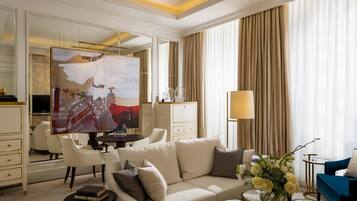Una habitación de hotel moderna con un espejo grande, un sofá color beige, un sillón azul y un área de comedor con una mesa y sillas.