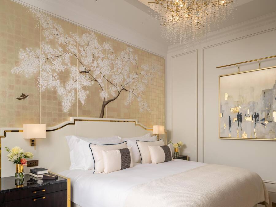 A hotel room with a large bed, two bedside tables, a wall-mounted artwork, and a chandelier.