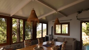 Une table à manger en bois, des chaises, un canapé et de grandes fenêtres donnant sur la forêt.