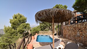 Un espace piscine avec des chaises longues, un mur en pierre et un parasol en chaume.