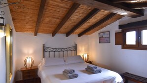 Une chambre avec un plafond en bois, un lit recouvert de draps blancs, deux lampes de chevet et un banc en bois.