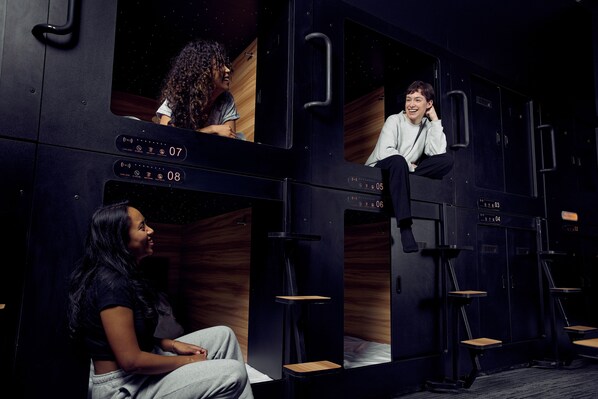 A modern, dark-themed room with individual compartments, each featuring a small table and a bench. - Capsule Hotel (Montréal)