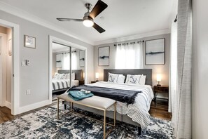 Un dormitorio moderno con una cama grande, un banco, un ventilador de techo y obras de arte en las paredes.