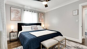 Un dormitorio con cama, mesitas de noche, ventilador de techo y obras de arte en las paredes.