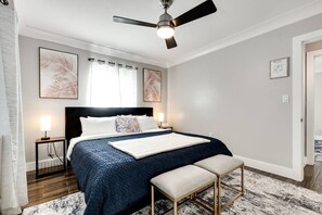 Un dormitorio con cama, mesitas de noche, ventilador de techo y obras de arte en las paredes.