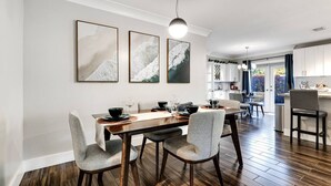 A modern dining area with a wooden table, grey upholstered chairs, and three framed artworks on the wall. - Royal Palms Beach Bungalow – A Tranquil Escape (Fort Lauderdale)