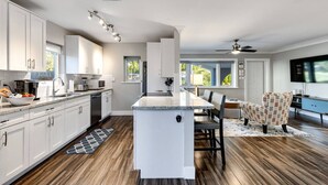 A modern kitchen with white cabinetry, a central island, and a dining area with a patterned chair. - Royal Palms Beach Bungalow – A Tranquil Escape (Fort Lauderdale)