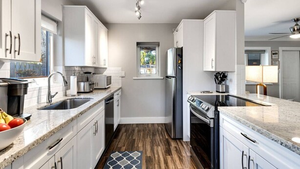 A modern kitchen with white cabinets, stainless steel appliances, and a granite countertop. - Royal Palms Beach Bungalow – A Tranquil Escape (Fort Lauderdale)