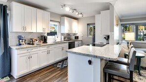Una cocina moderna con armarios blancos, encimera de granito y una isla integrada con taburetes de bar.