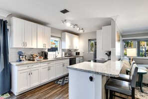 Una cocina moderna con armarios blancos, encimera de granito y una isla integrada con taburetes de bar.