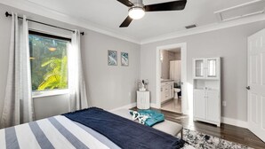 A bedroom with a bed, a ceiling fan, a window with curtains, and a view of a bathroom. - Royal Palms Beach Bungalow – A Tranquil Escape (Fort Lauderdale)
