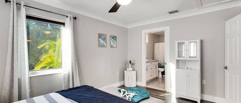 A bedroom with a bed, a ceiling fan, a window with curtains, and a view of a bathroom.