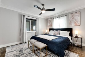 Une chambre à coucher comprenant un lit, des tables de chevet, un banc, un ventilateur de plafond et des œuvres d’art accrochées aux murs.
