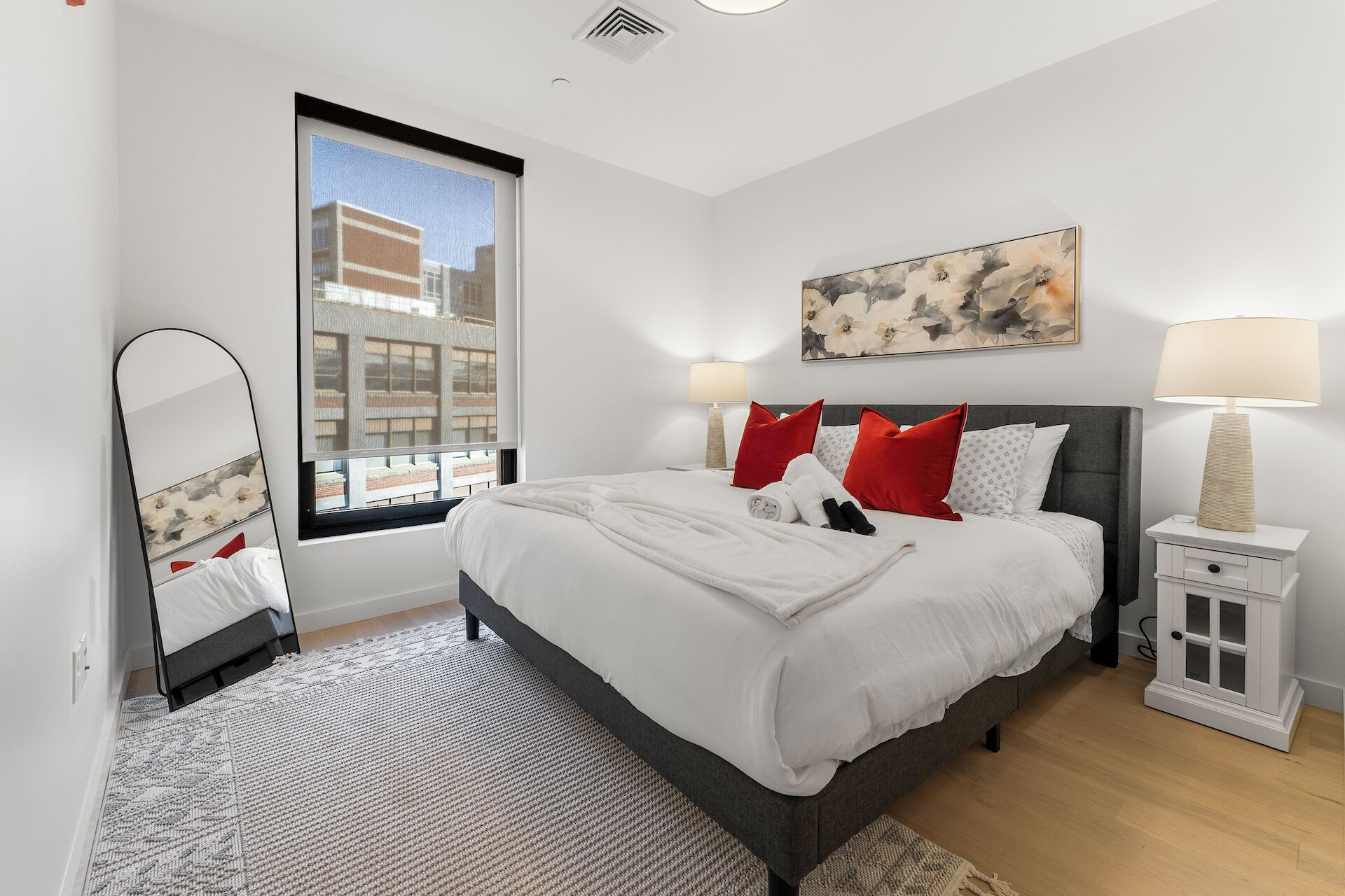 Een moderne slaapkamer met een groot bed, een nachtkastje, een spiegel en een raam met uitzicht over de stad.