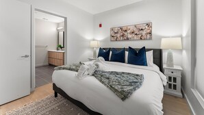 Een moderne slaapkamer met een groot bed, twee bedlampen, een nachtkastje, een kapstok en een schilderij aan de muur.