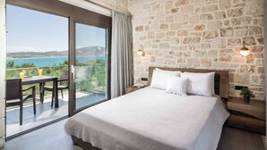 A bedroom with a large bed, a view of the sea, and a balcony with a table and chairs.