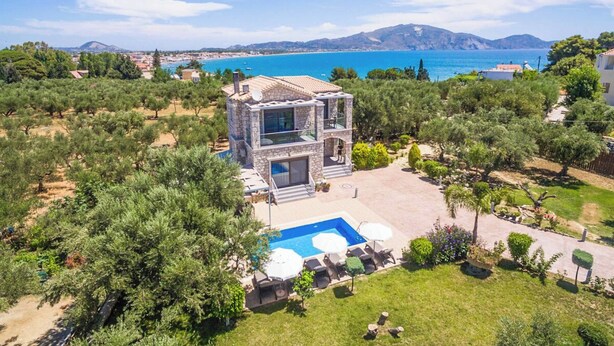 A modern villa with a pool, surrounded by lush greenery and a scenic coastal view.