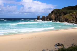 Une plage aux eaux turquoise et limpides, bordée de falaises rocheuses et d’un rivage sablonneux.