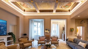 A spacious living room with a high ceiling, ornate ceiling details, and a large flat-screen TV. - Palazzo Doni by Florence Art Apartments (Florence)