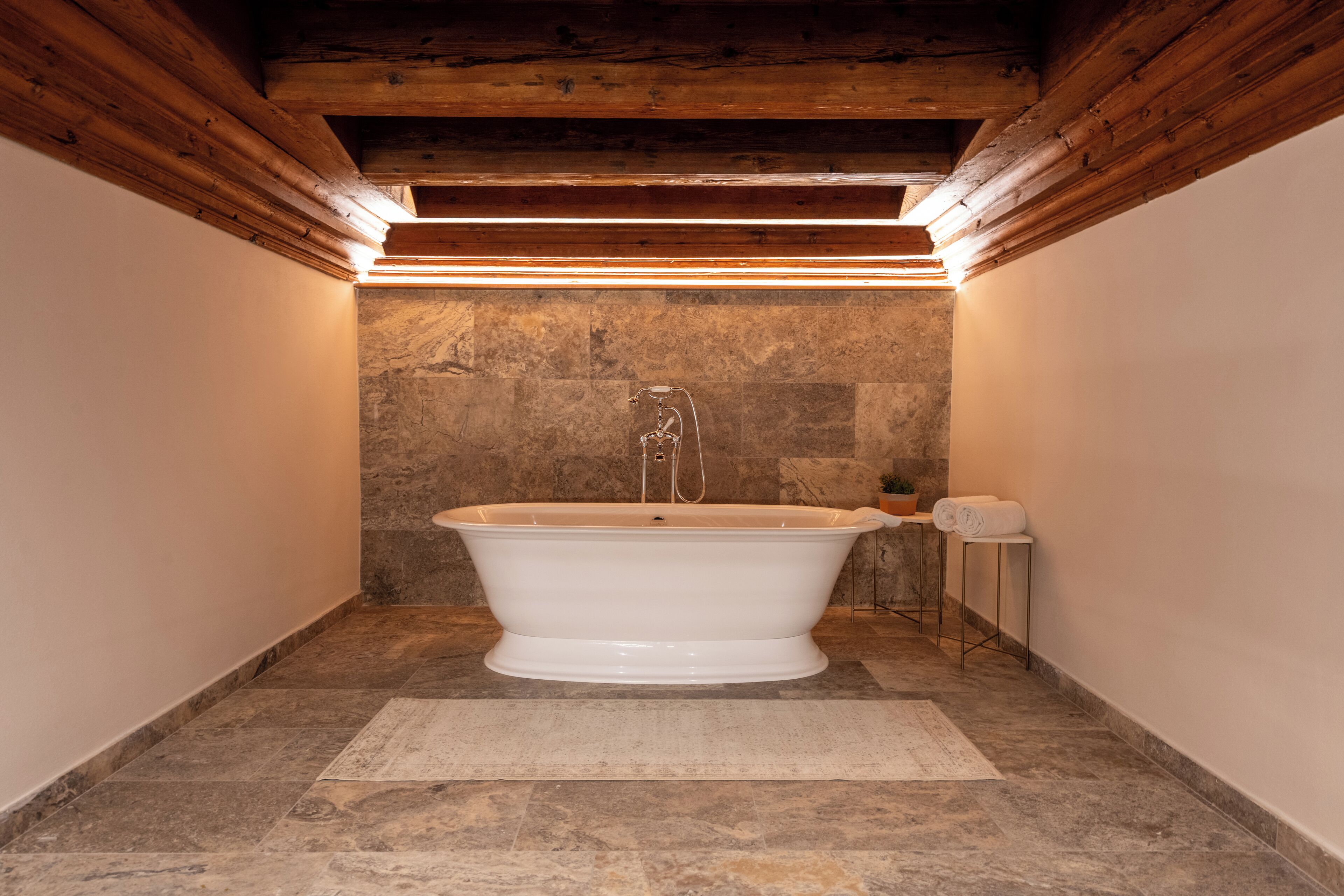 Une salle de bain avec une baignoire sur pieds, des murs en pierre et des poutres en bois au plafond.