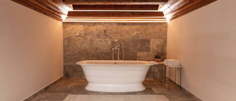 Une salle de bain avec une baignoire sur pieds, des murs en pierre et des poutres en bois au plafond.