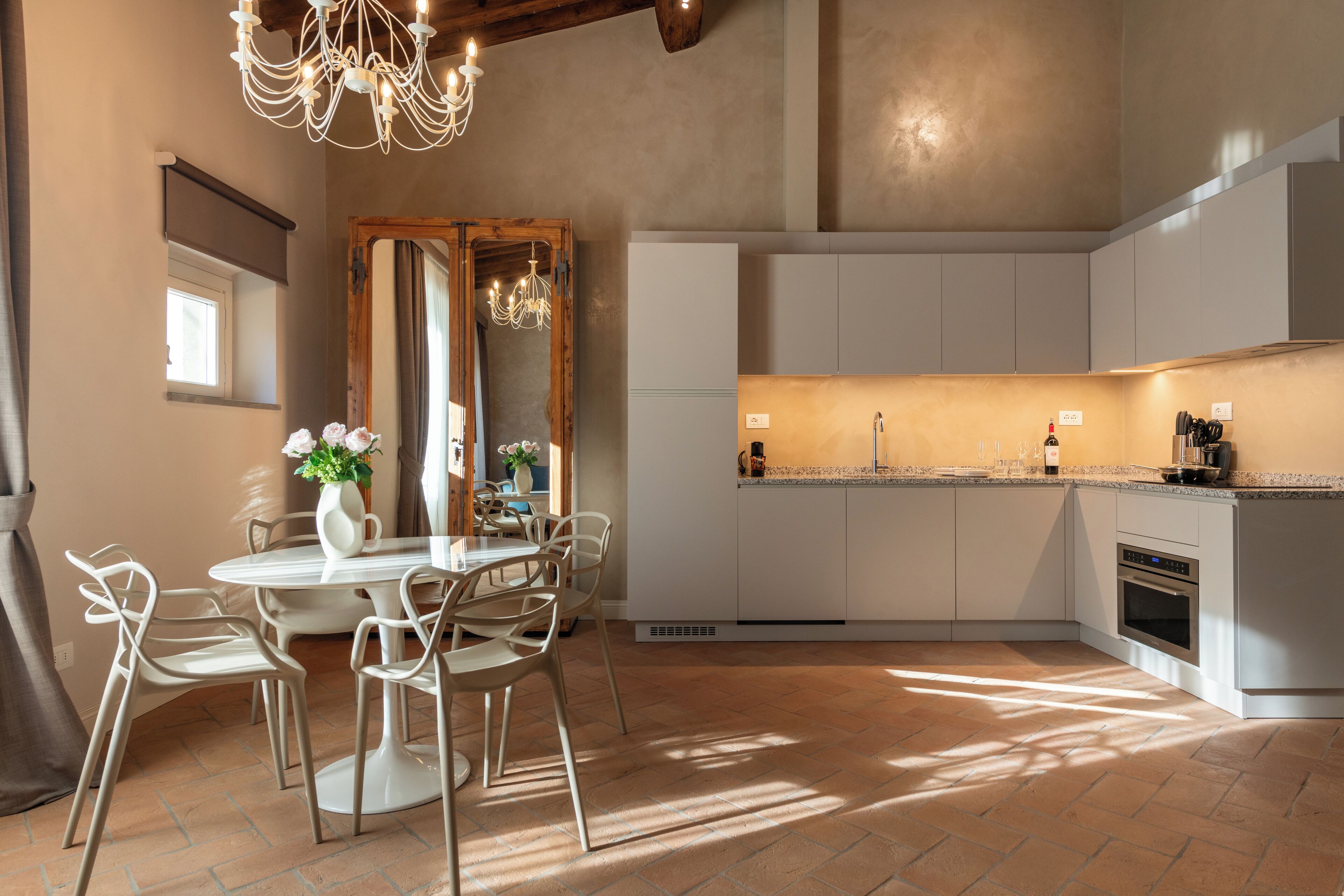 A modern kitchen with white cabinets, a built-in oven, and a dining area with a round table and chairs.