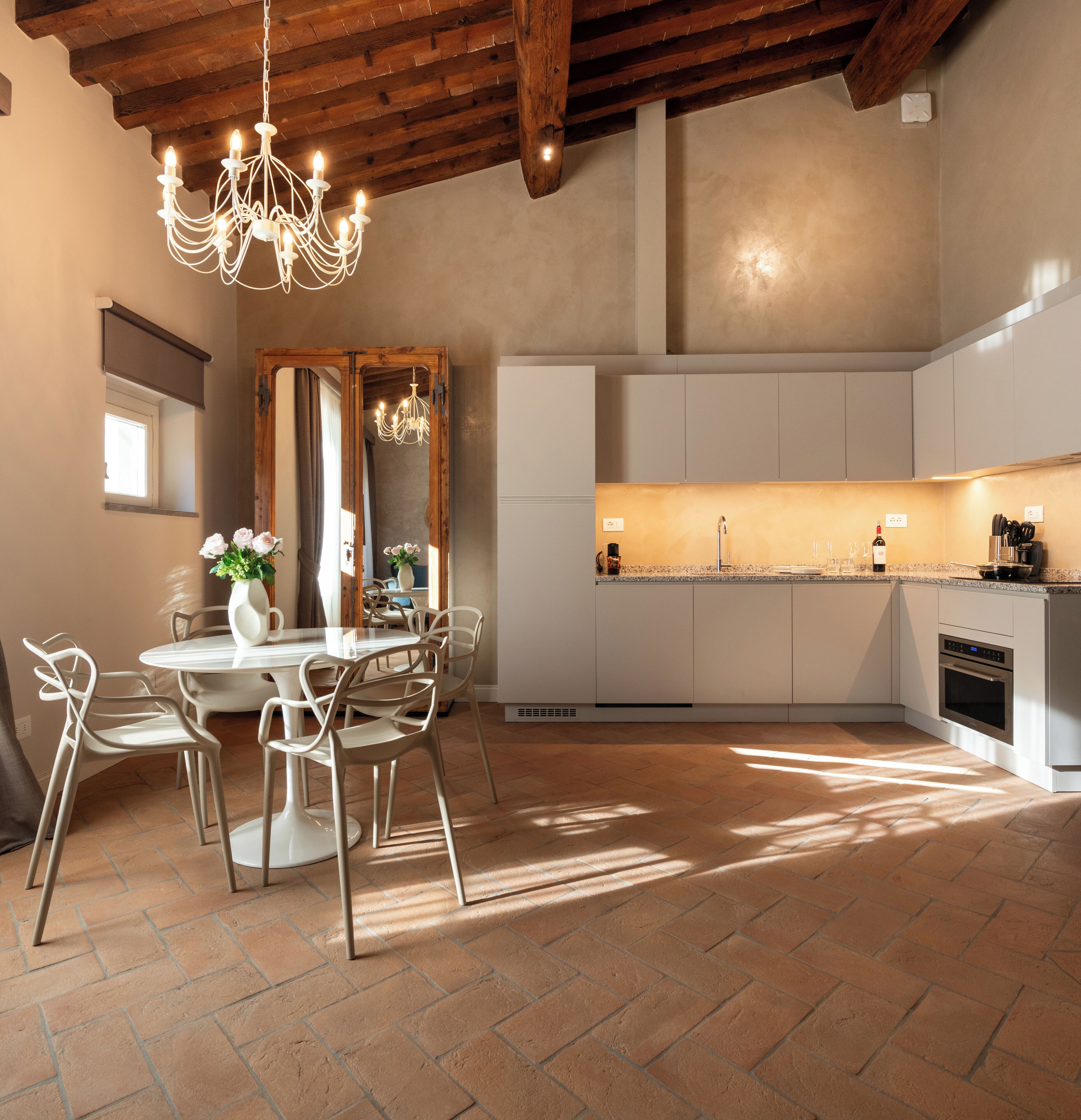 A modern kitchen with white cabinets, a built-in oven, and a dining area with a table and chairs.