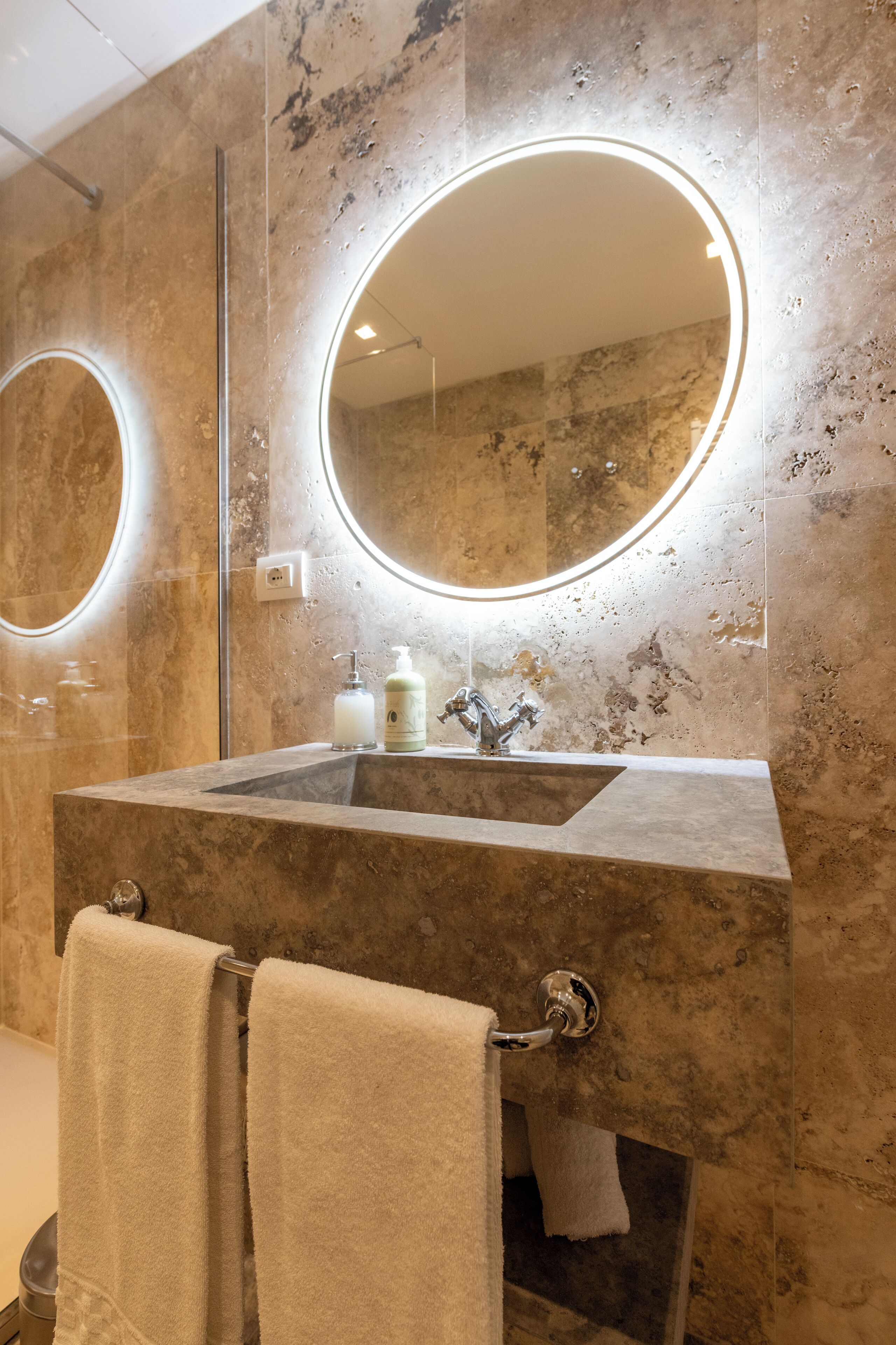 A bathroom with a marble sink, two round mirrors, and a towel rack.