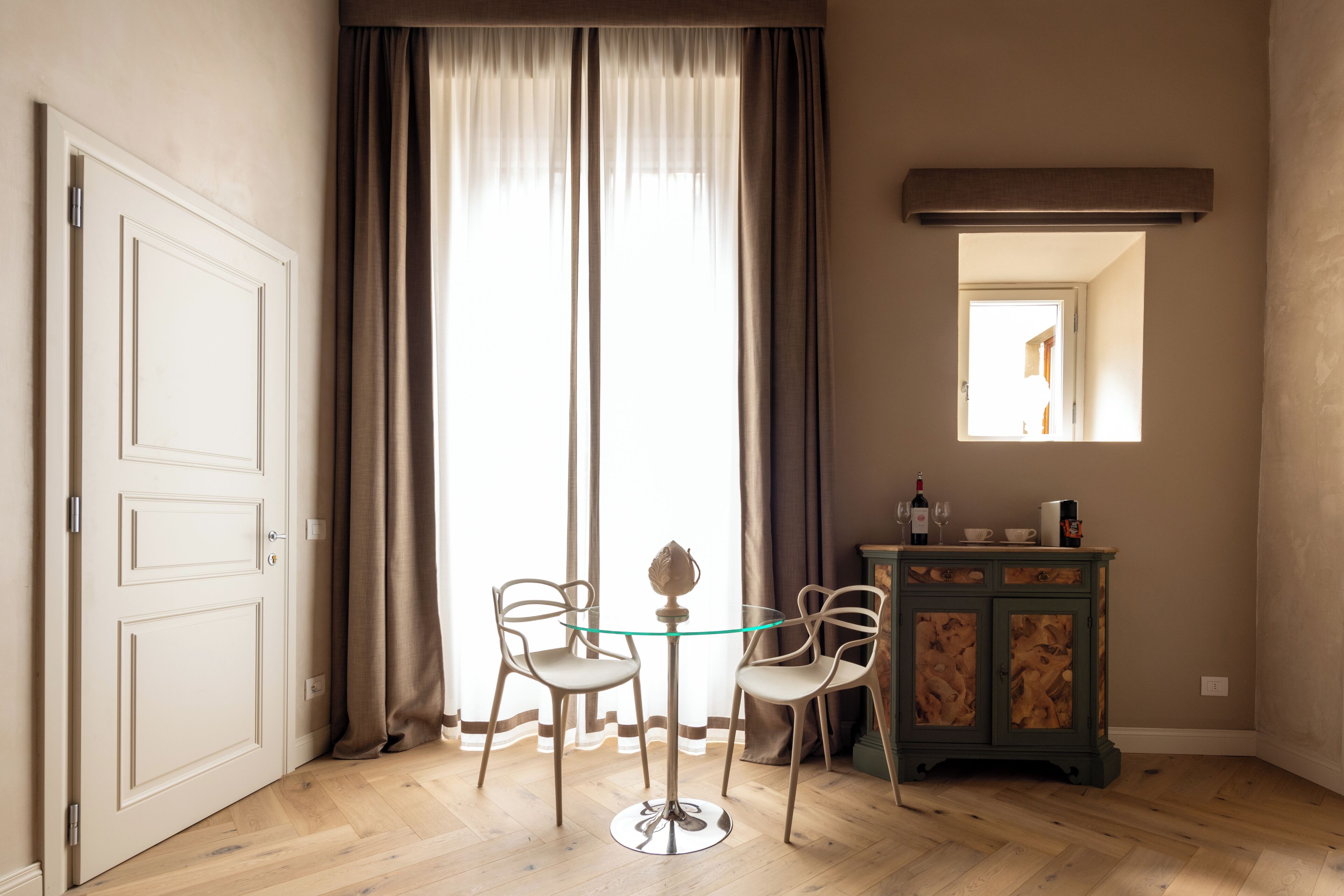Ein Zimmer mit Holzboden, einem Glastisch mit zwei Stühlen, einem Schrank mit Spiegel und einer Tür.