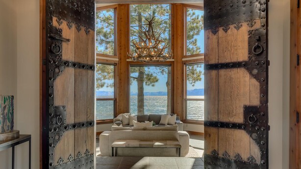 Una habitación con un gran puerta de madera que da a una zona de estar con vista a un cuerpo de agua y árboles.