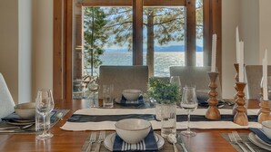 Mesa de comedor para dos con vista al mar y a los árboles a través de amplios ventanales.