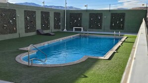 A swimming pool with a surrounding grassy area and a wall with planters.
